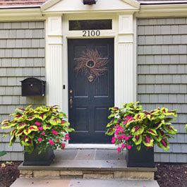 Two black square planters on front doorsteps display - coleus and pink impatiens