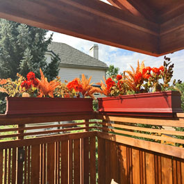 Red PVC planters on top of redwood backyard fencing with beautiful fall display and red flowers