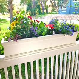 Rail top planter straddling rail with yellow daisys, and assortment of red, blue, and purple flowers