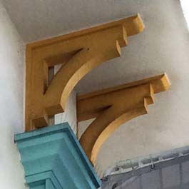 painted yellow wood brackets with curved beam and backer boards