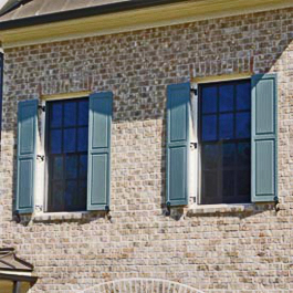 light blue raised panel shutters hinged on brick home